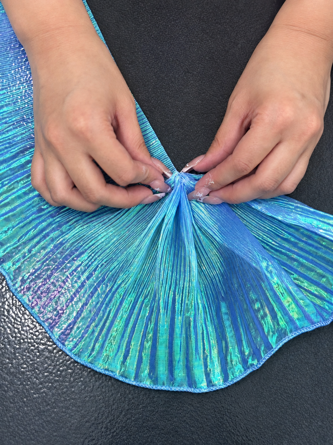 Hands gathering iridescent pleated material into a sculptural fan